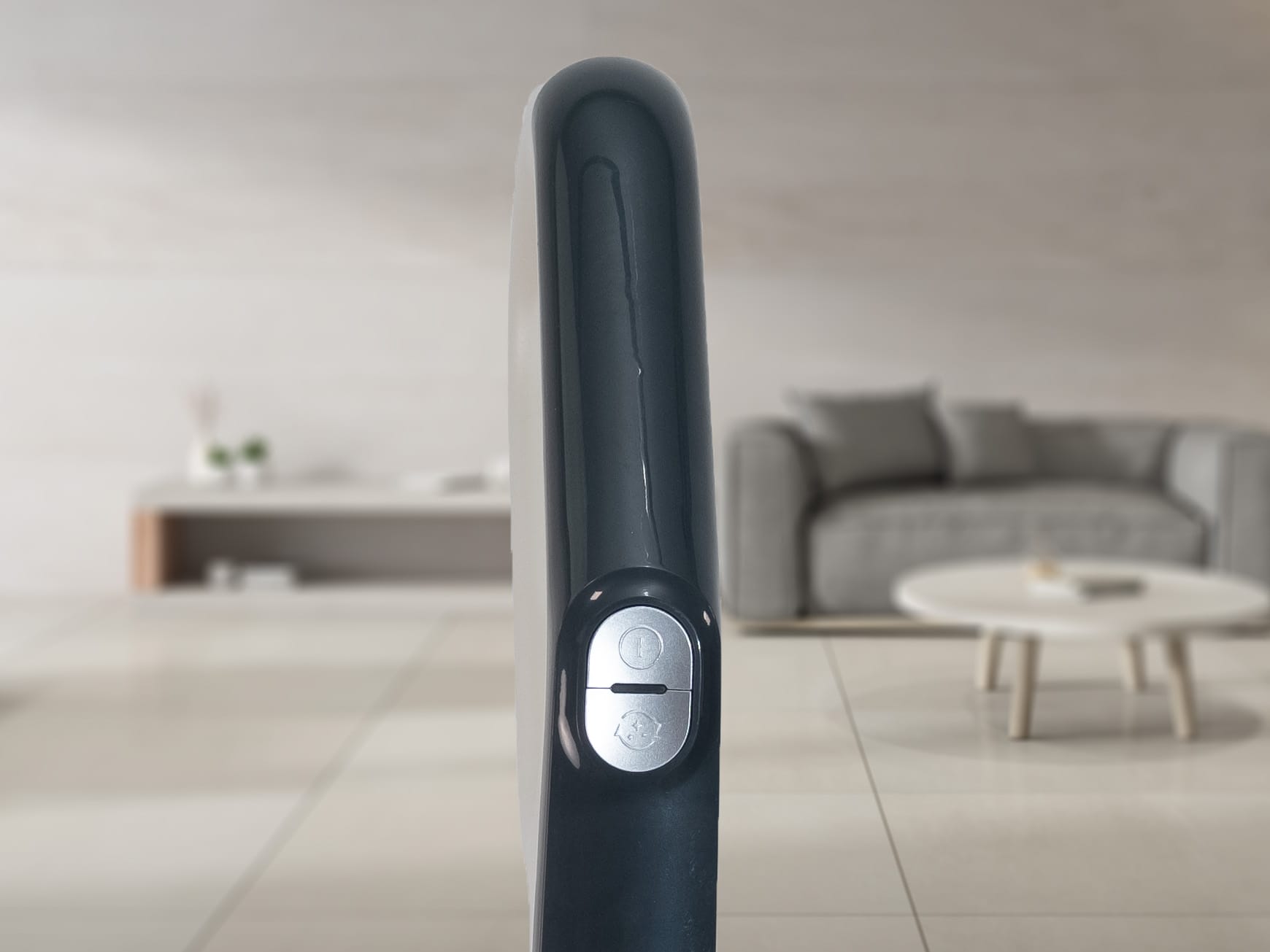 Nahaufnahme der Seite eines dunkel gefärbten elektronischen Geräts mit einer Einschalttaste vor dem verschwommenen Hintergrund eines modernen Wohnzimmers mit Sofa und Couchtisch.